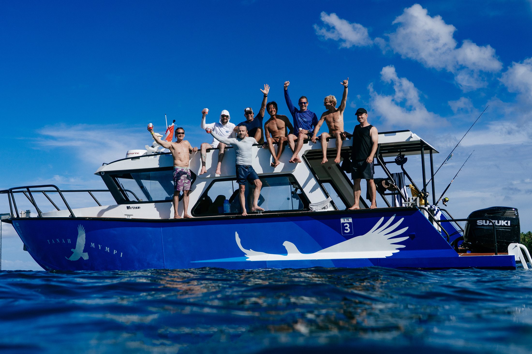 A group of eight guests aboard the Tanah Mympi speedboat, waving and celebrating on the water